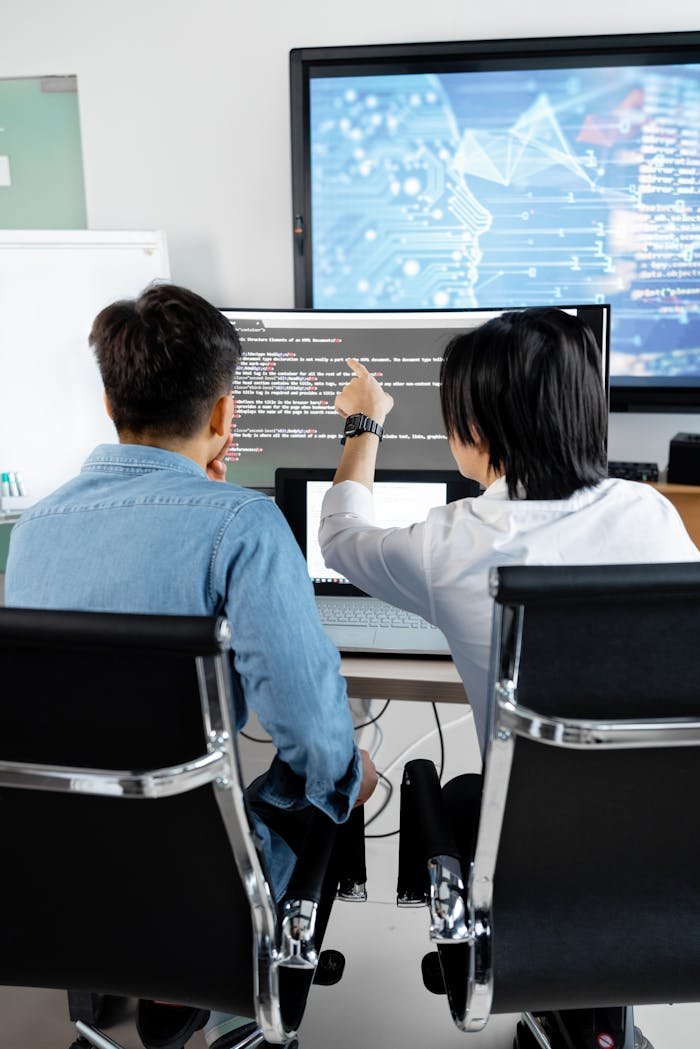 Two adults collaborating in an office, discussing code on a computer screen.